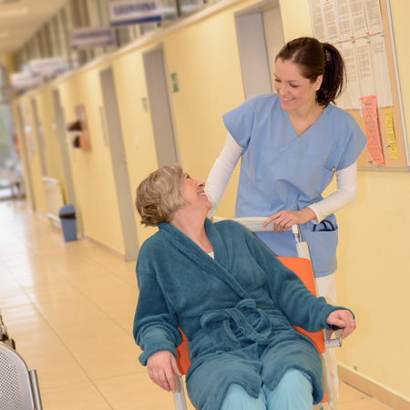 Smiling young female nurse in hospital taking care of senior patient in wheelchairの写真素材