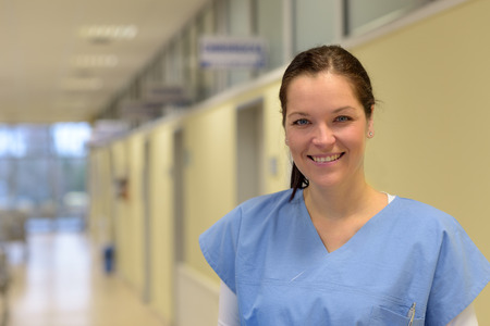 Smiling young female nurse in hospital standing alone in hallwayの写真素材