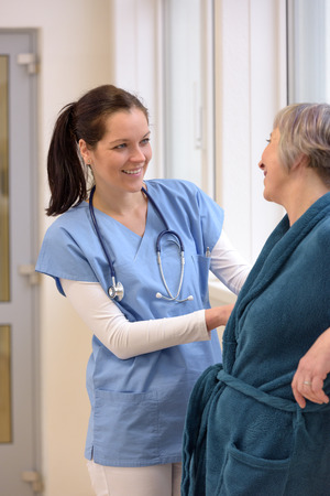 Smiling female nurse helping senior patient in hospital corridorの写真素材