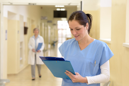 Smiling young female nurse in hospital looking down at patient filesの写真素材