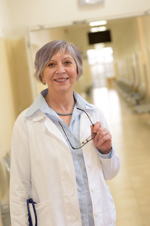 Senior doctor standing in hospital corridor smilingの写真素材