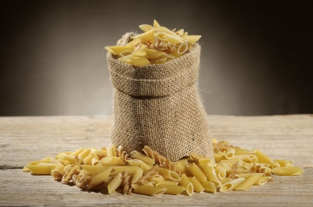 jute bag with variety of uncooked pasta on wooden tableの写真素材