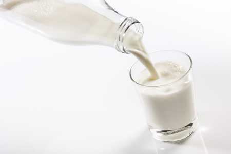 glass bottle pouring milk into a glass on white backgroundの写真素材