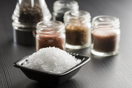 black bowl with coarse salt with variety of salt on black tableの写真素材