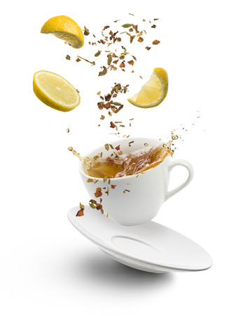cup of tea jumps with herb tea and lemon slices splashing on white backgroundの写真素材