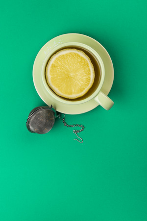 cup of tea with lemon slice and infuser on green tablecloth.の写真素材