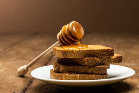 Honey dipper resting on some wholemeal rusks on table.