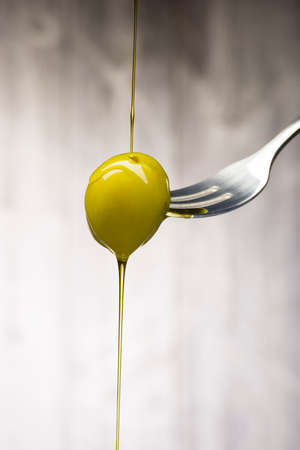Green olive on fork with dripping oil, on wooden backgroundの写真素材