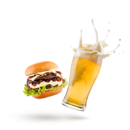 Glass of lager beer with hamburger jumping on white background.の写真素材