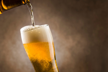 Pouring lager beer into glass with foam on dark background.の写真素材