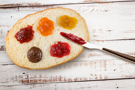 Slice of white bread with variety of jam spread and knife. Top view on wooden table.の写真素材
