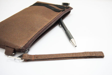 A grey pencil is taken out of brown pencil bag on a white background.