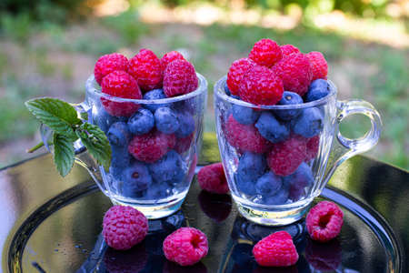 raspberries and blueberries in transparent cups in the gardenの写真素材