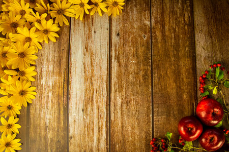 wooden background decorated with yellow autumn flowers and red apples, autumn conceptの写真素材