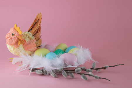 Toy handmade hen with a nest of colored eggs decorated with pussy willow on a pink background