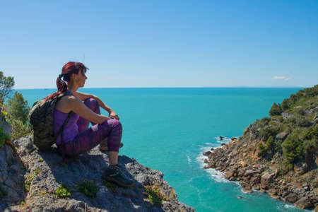 Woman trekker sits on the top of the mountain above the seaの写真素材