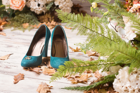 Wedding rings on green suede shoes. Wooden background with autumn leaves and green fern.の写真素材