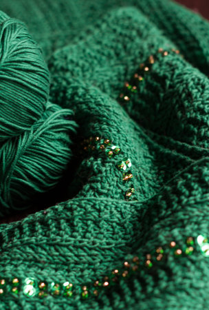 Two balls of green yarn and green beaded scarf lays on a dark wooden table. Yarn is deep green....