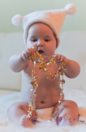 Baby in hat plays with gold tinselsの写真素材