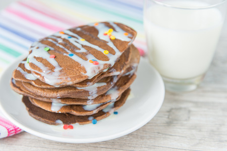 Decorated chocolate pancakes with the glass of milk on the coloured napkinの写真素材