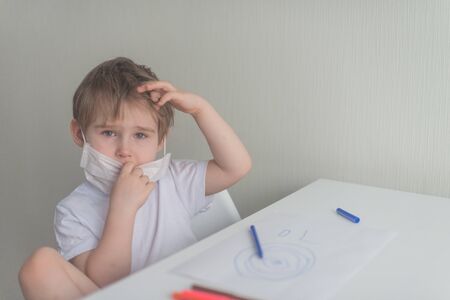 Little boy sits near the table and touch the medical maskの写真素材