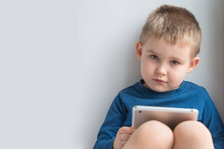 Adorable 4 years old boy portrait in blue longsleeve holding tab gadgetの写真素材