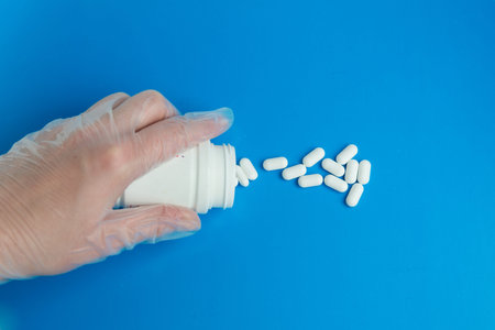The doctors gloved hand pours white pills out of a jar