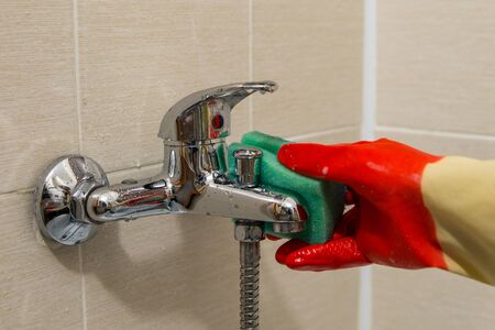 Hand in rubber glove cleans dirty calcified shower mixer tap, close up photoの写真素材