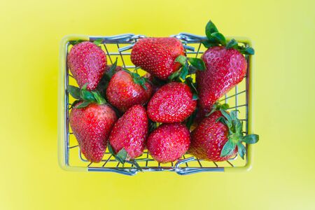 fresh strawberries with a shopping basket on a bright yellow background. advertising concept for fresh productsの写真素材