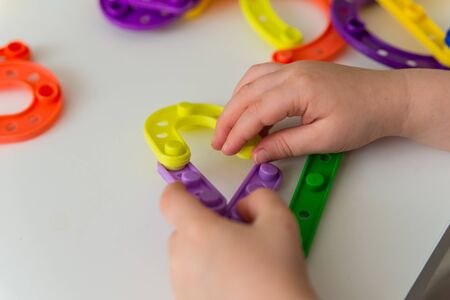 Close up of kid hands playing bright plastic toy constructor. Creative baby make new formsの写真素材