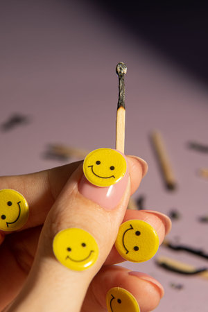 A burnt match in a hand among many matches on a light purple background. Yellow emoticons, creative.