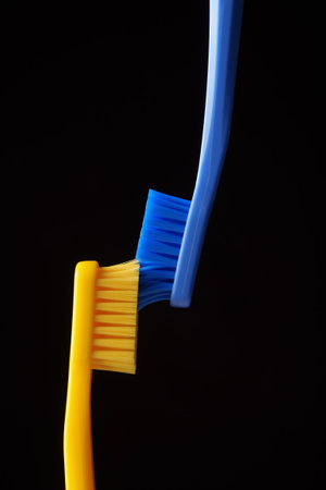 Two yellow and blue plastic toothbrushes on a black background.の写真素材