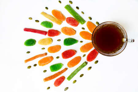 Black tea in a glass cup with colorful pineapple candies and pumpkin seeds on a white backgroundの写真素材