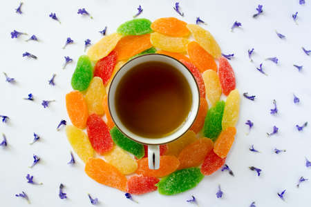 Cup of tea with candied fruits and small blue flowers on a white backgroundの写真素材