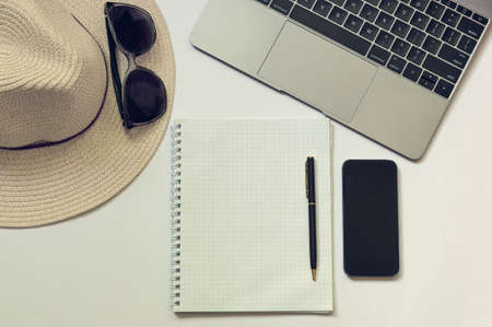 Workplace of a blogger, writer or freelancer with a laptop, open notebook, phone, pen, hat. White background with copy space.Toned photo. View from aboveの写真素材