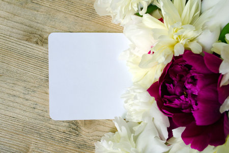 Flowers peonies white and lilac colors with a note on a wooden table. Mock up for greeting card