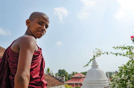 Dickwella, Sri Lanka, 04-15-2017: Young Buddhist monk on the background of a Buddhist pagoda looks at the cameraのeditorial素材