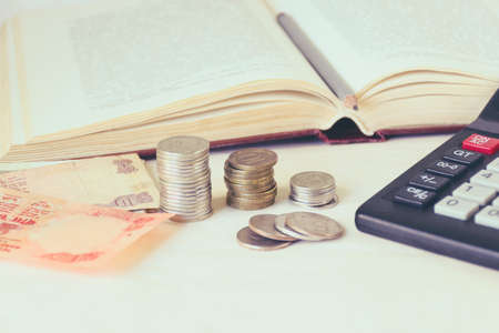 Money banknote, coins in piles, a calculator in front of an open book. The concept of expensive education and low scholarship. Toned imageの写真素材