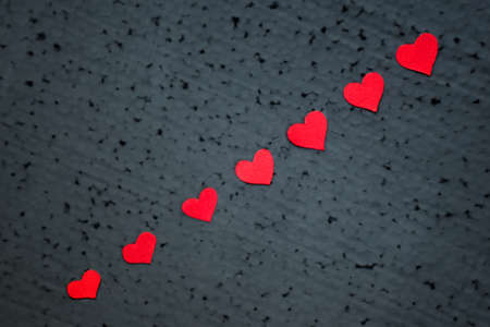 Small red hearts are arranged diagonally on a black background.の写真素材