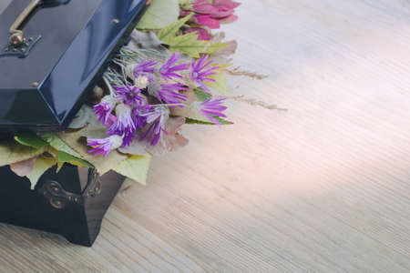 An old black box with an open lid, under which are autumn leaves and wildflowers. Wooden background. Autumn composition. Side view. Place for textの写真素材