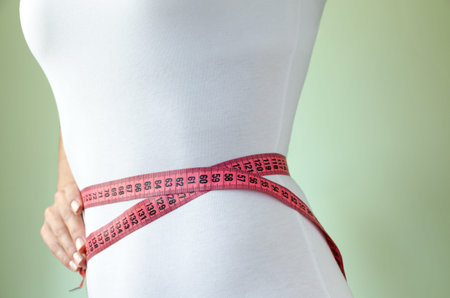 Waist of young, sporty slender girl in white underworld, wrapped in measuring tape. The concept of...