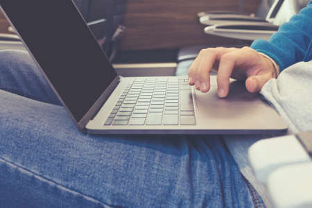 Hand of a young man in jeans working on a laptop in transport close-upの写真素材