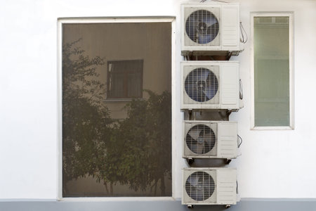 A lot of air conditioners are hanging next to wall near the window.