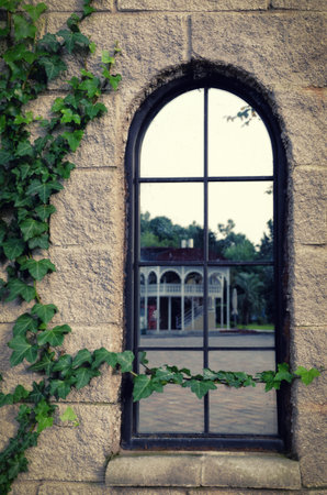 A high mirror window in an old house in which another building is reflected. The walls are covered...