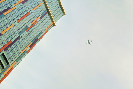 Plane flies on the background of a skyscraper with colorful windows. City life.