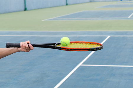 Concept of sport and active lifestyle - tennis court, hand holds tennis racket with ball.