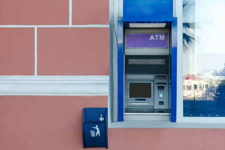 ATM in the wall of the building near the window, near it a small trash can and checks. Empty copy space for text.の写真素材