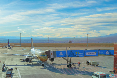Tbilisi, Georgia, 2017-12-07: Airplane of Gulf Avia in Tbilisi airport with jetwayÂ ramp waiting for passengers, in background beautiful Georgian landscape.のeditorial素材