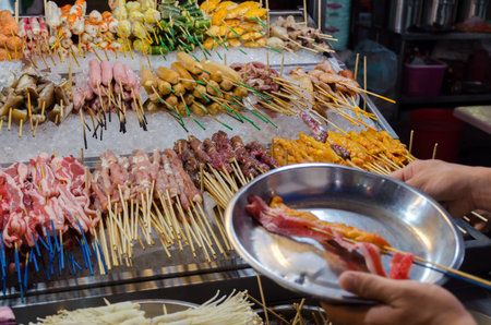 Counter with Chinese street food, the buyer fills a plate with bacon. Tourist food market. Malaysia, Kuala lumpur, Jalan Alor.の写真素材