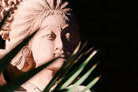 Traditional Balinese sandstone young woman statue portrait, illuminated by the sun among the palm trees. Place for text, copy space.の写真素材